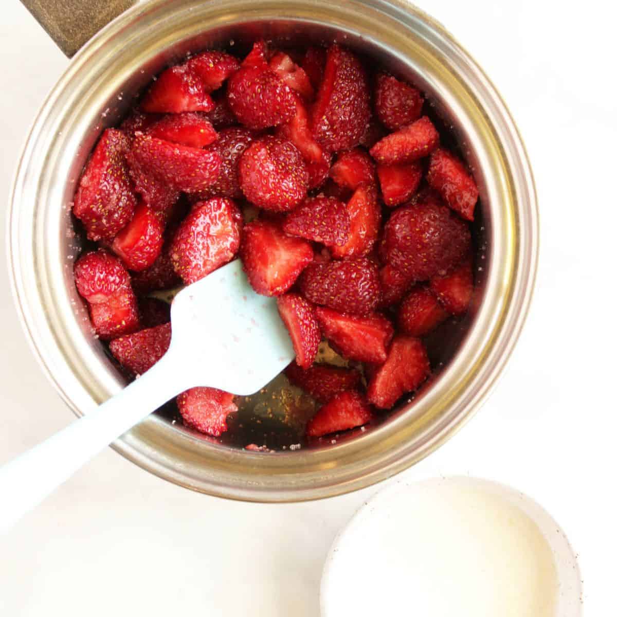 pale blue spatula stirs fresh berry chunks in small saucepan.