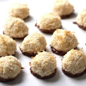 several golden balls spiked with flaked coconut and bottoms coated with chocolate all sitting randomly on white surface.