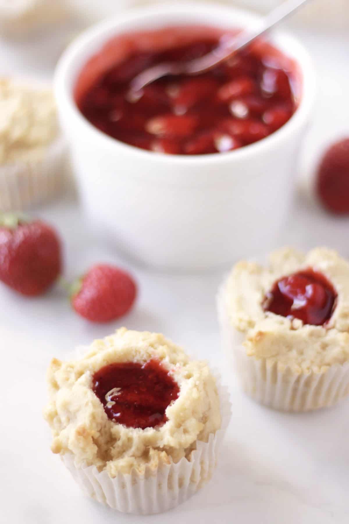 strawberry filled vanilla cupcakes with whole berries and white ramekin of remaining filling behind them.