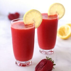 two glasses of deep pink slushie garnished with slices of lemon.