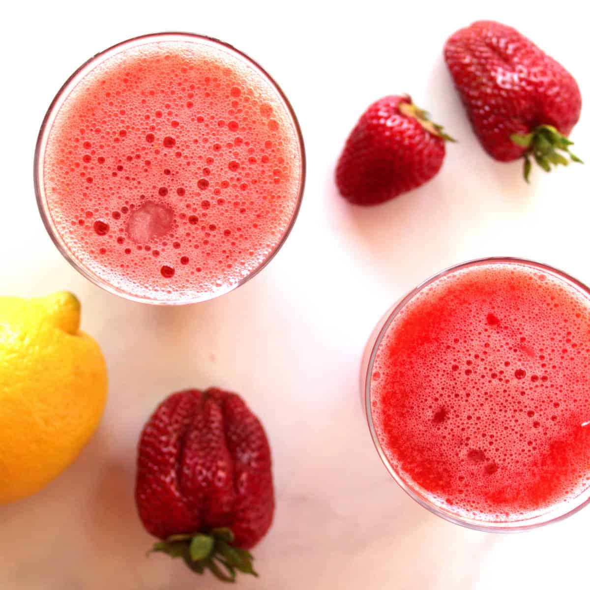 looking down into two glasses of pink slushie drinks, with whole strawberries and a lemon nearby.