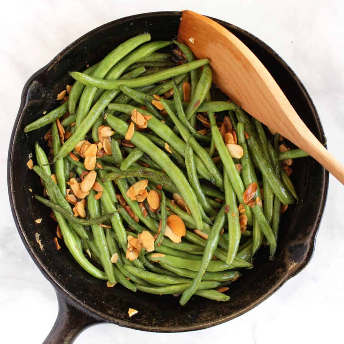 fresh green beans added to cast iron skillet with browned almonds.