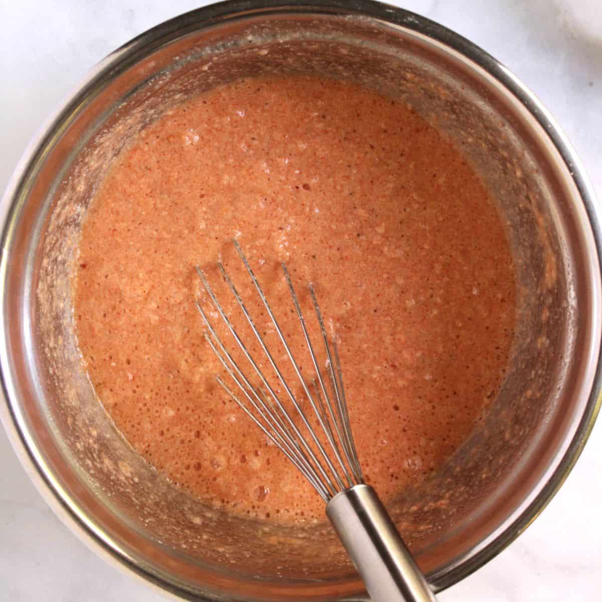 whisk in thin reddish batter in a mixing bowl.