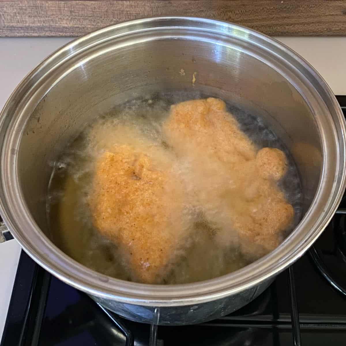 bubbles form around two pieces of golden, battered fish sizzling in hot oil in a pan.