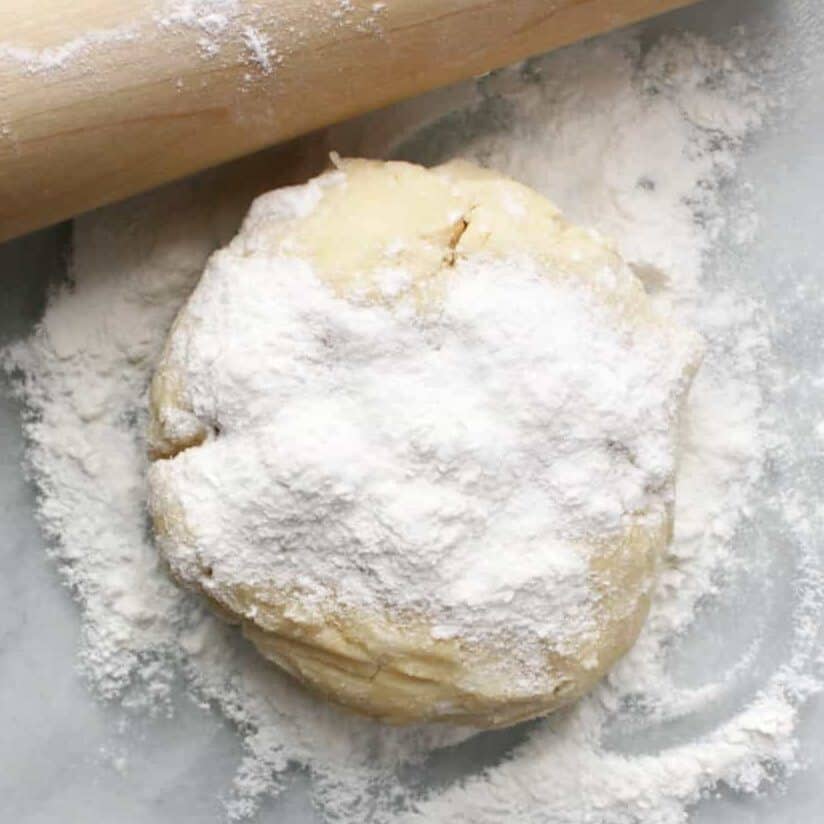 floured ball of pie dough on marble with wooden rolling pin