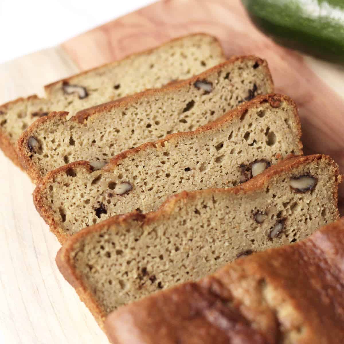 four slices of gluten free zucchini bread leaning away from loaf on wood plank.