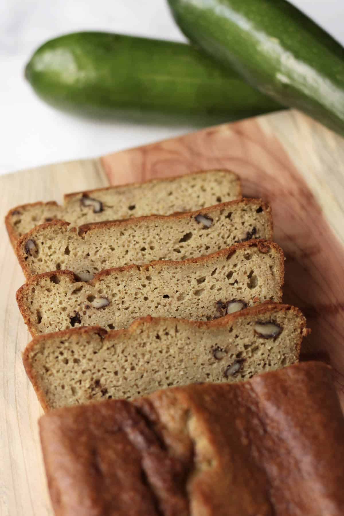 looking down on four slices of gluten free zucchini bread falling away from loaf, on wooden plank beside whole zucchini.