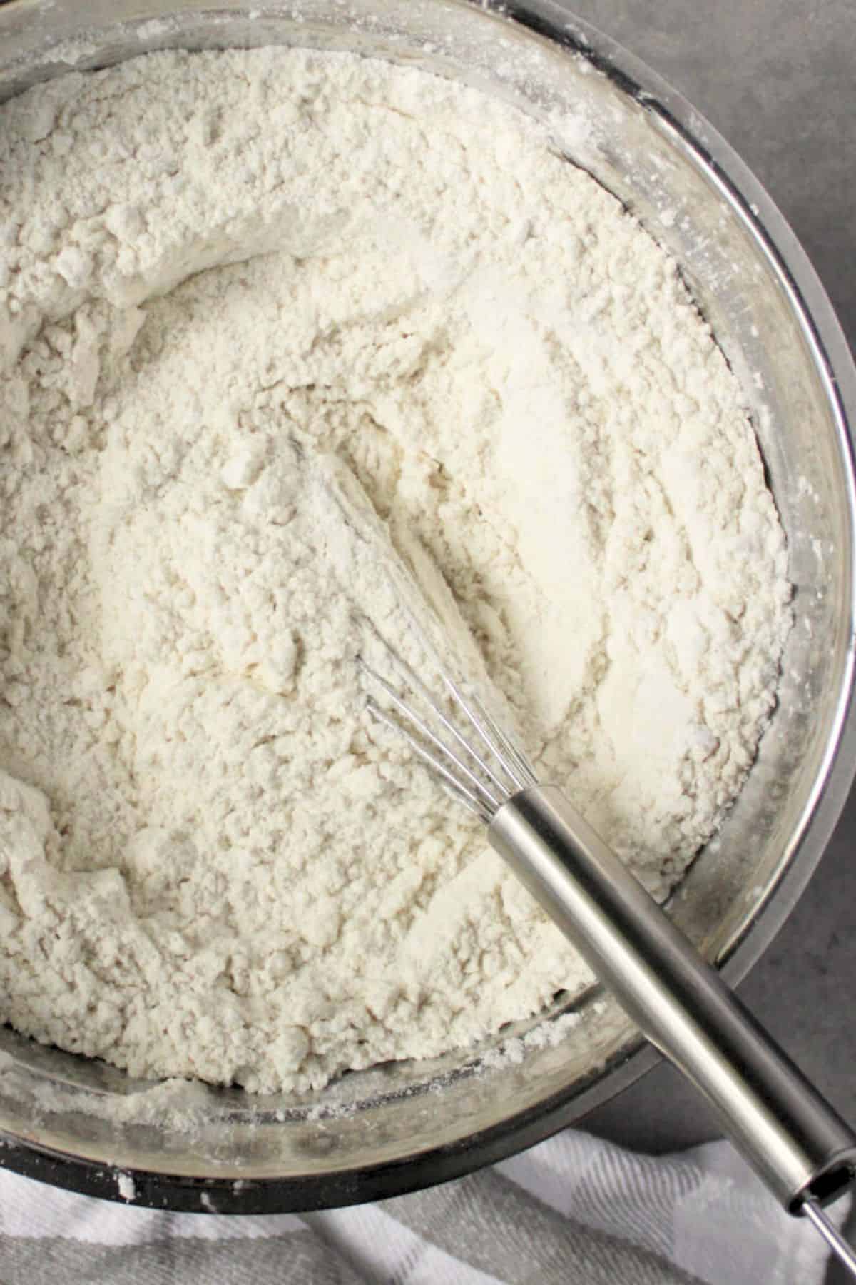 a wire whisk sits in a stainless steel bowl of sorghum flour.