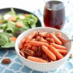 glazed carrots with pecans in white bowl by salad and maple syrup.