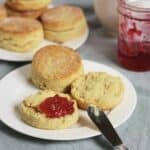 biscuit on white plate split open with butter and red jam on it.