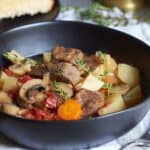 black bowl with chunks of stewed beef, carrots, potatoes, and mushrooms.