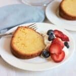 slice of gluten-free pound cake on white plate with whipped cream and berries.