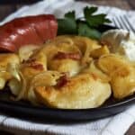 golden, fried pierogi on black plate with bacon, onions, and sausage.