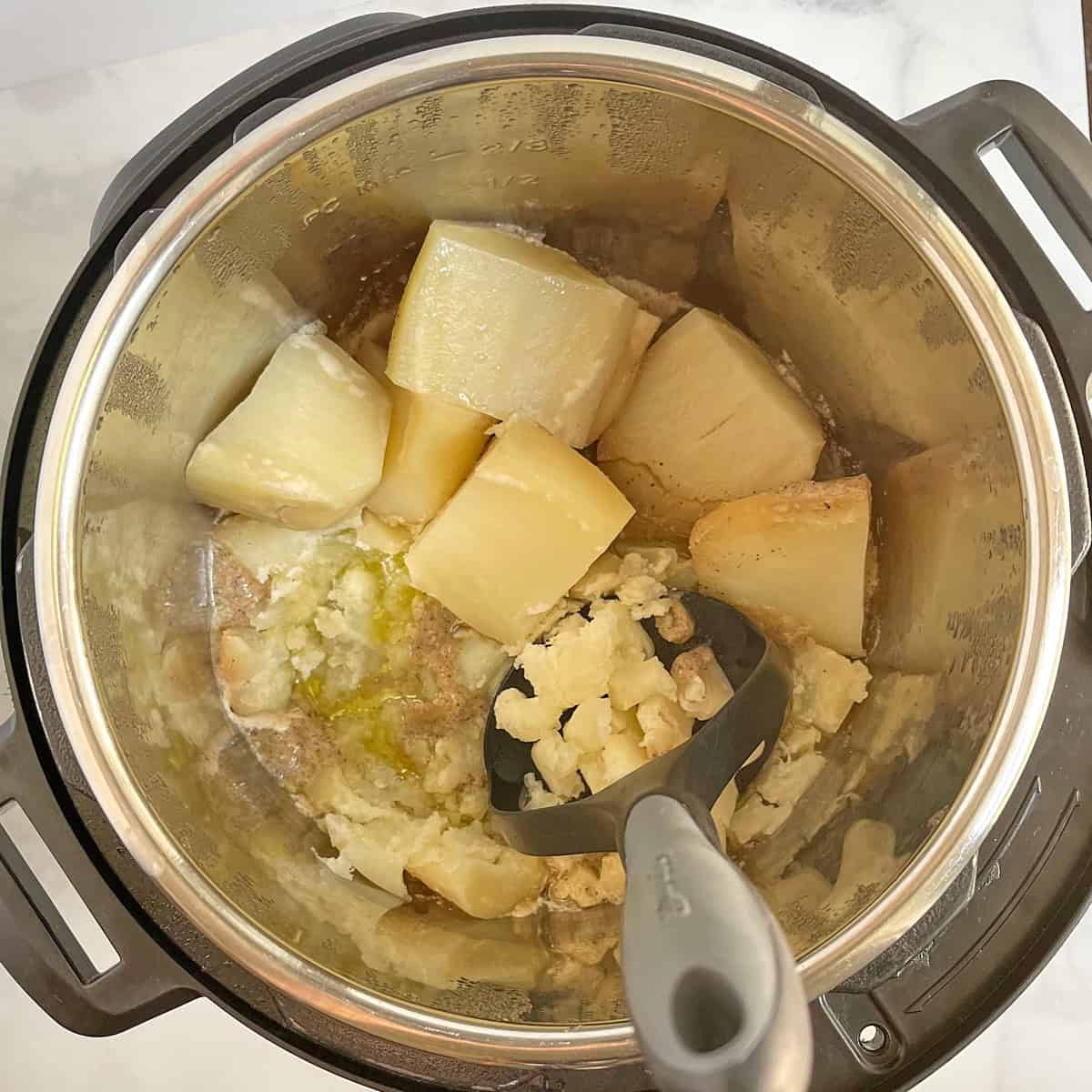 potato masher beginning to mash cooked potatoes with seasoned liquid in Instant Pot.