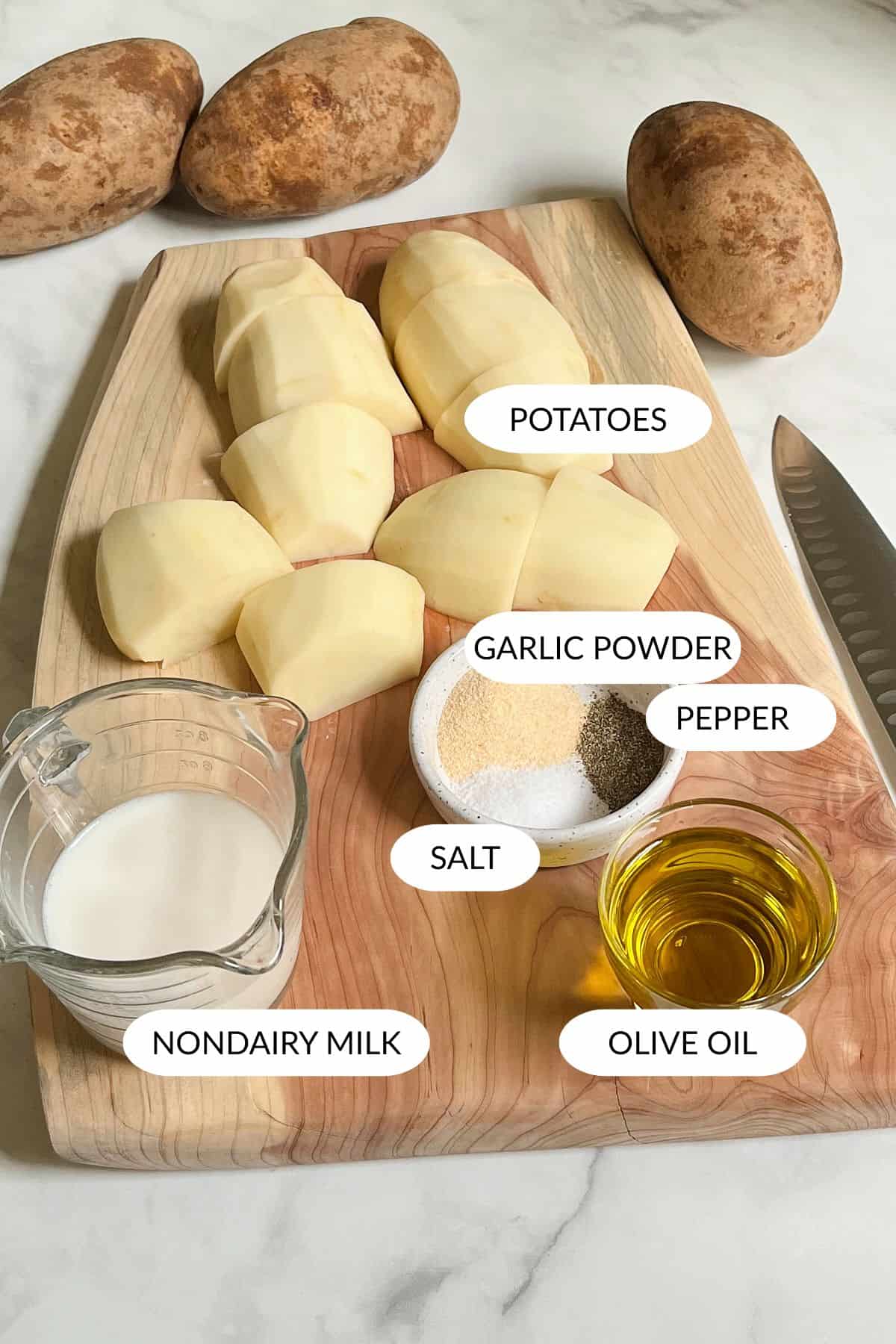 peeled potato chunks, spices, milk, and olive oil arranged on wooden board.