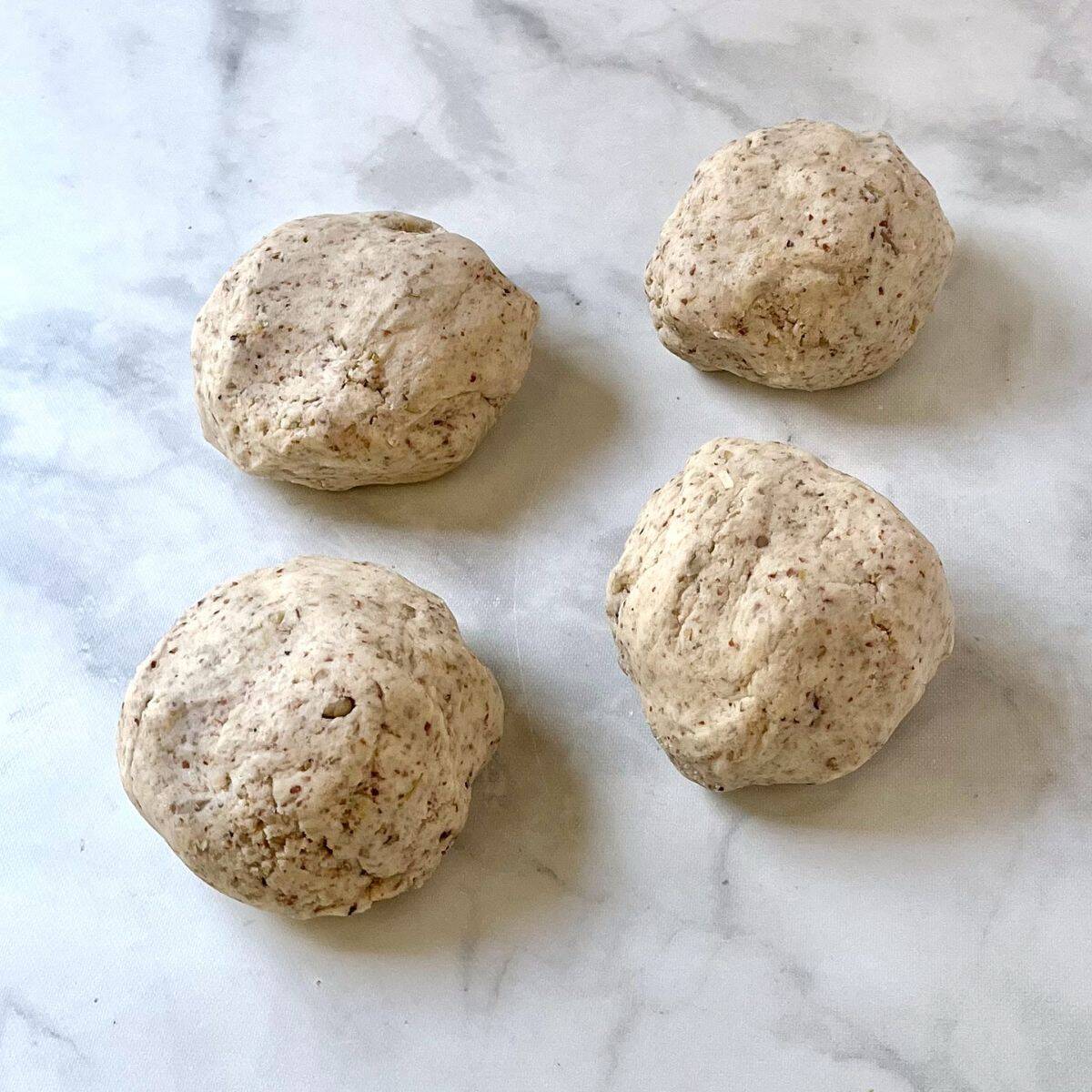 four balls of dough on marble counter.