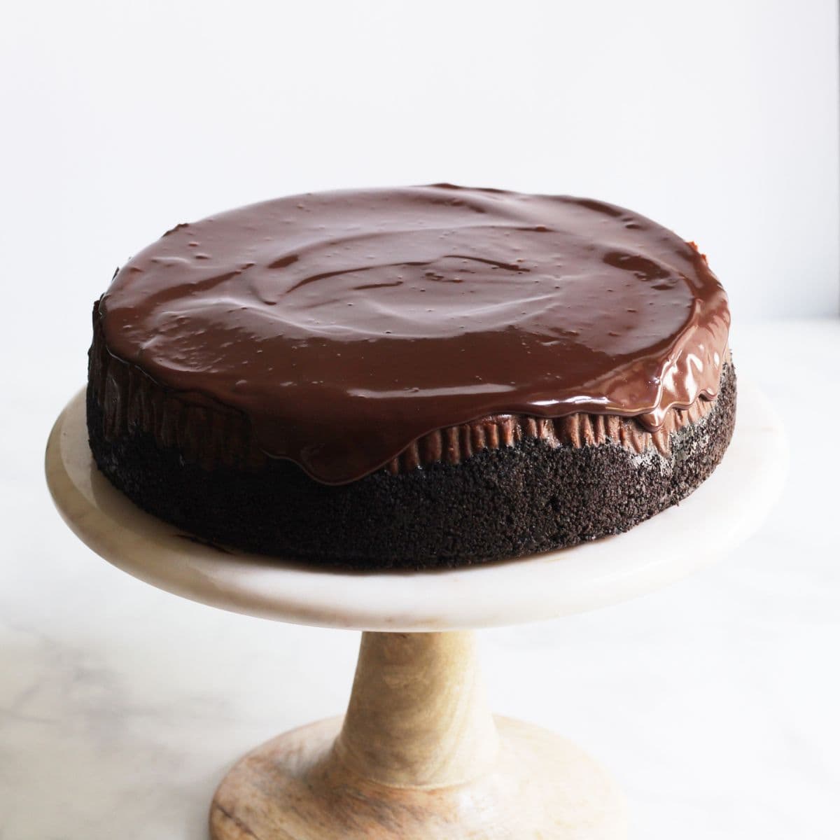 chocolate cheesecake on pedestal plate with shiny chocolate ganache on the top and running down sides.