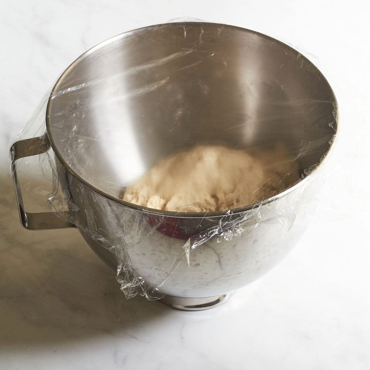 dough in mixing bowl covered with plastic film.