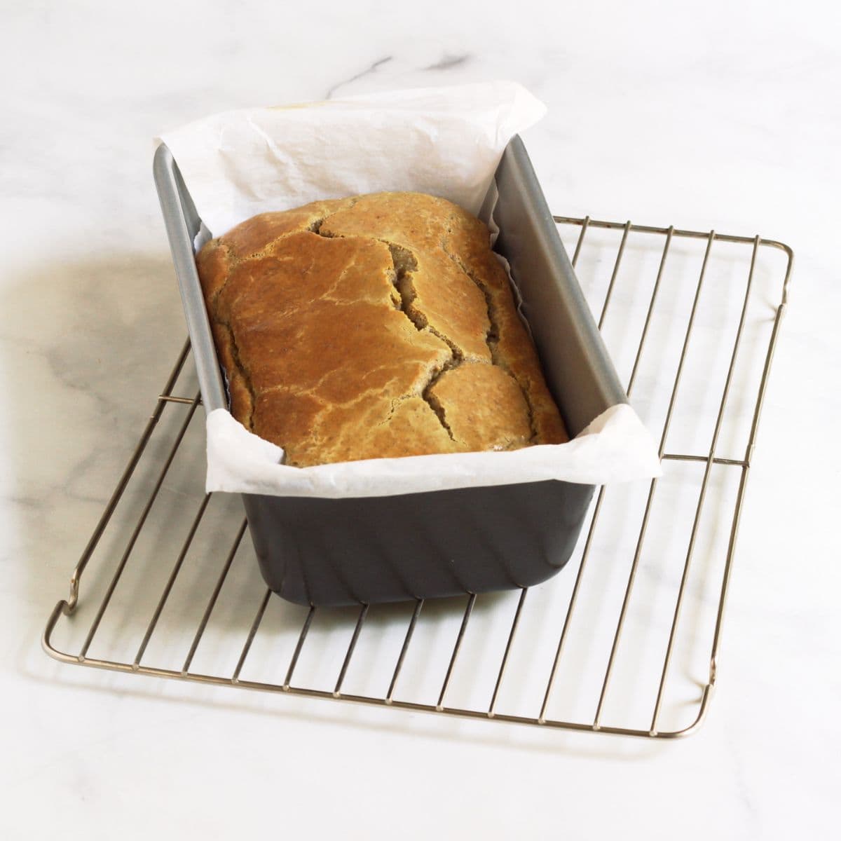 golden, baked loaf in pan on cooking rack.