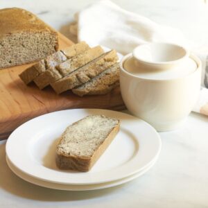 buttered slice of almond bread on white plate in front of remaining loaf.