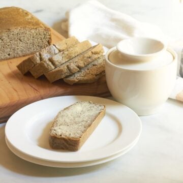 buttered slice of almond bread on white plate in front of remaining loaf.