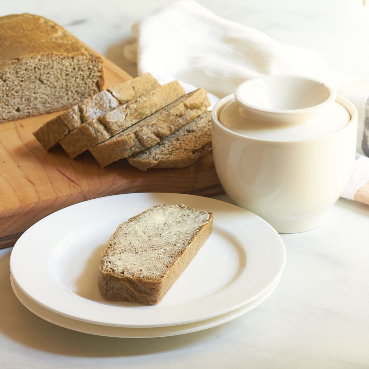 buttered slice of almond bread on white plate in front of remaining loaf.