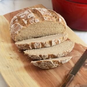 round crusty loaf of artisan bread, partially sliced, on wooden board.