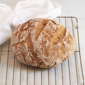 scored, crusty, golden round loaf on wire rack.