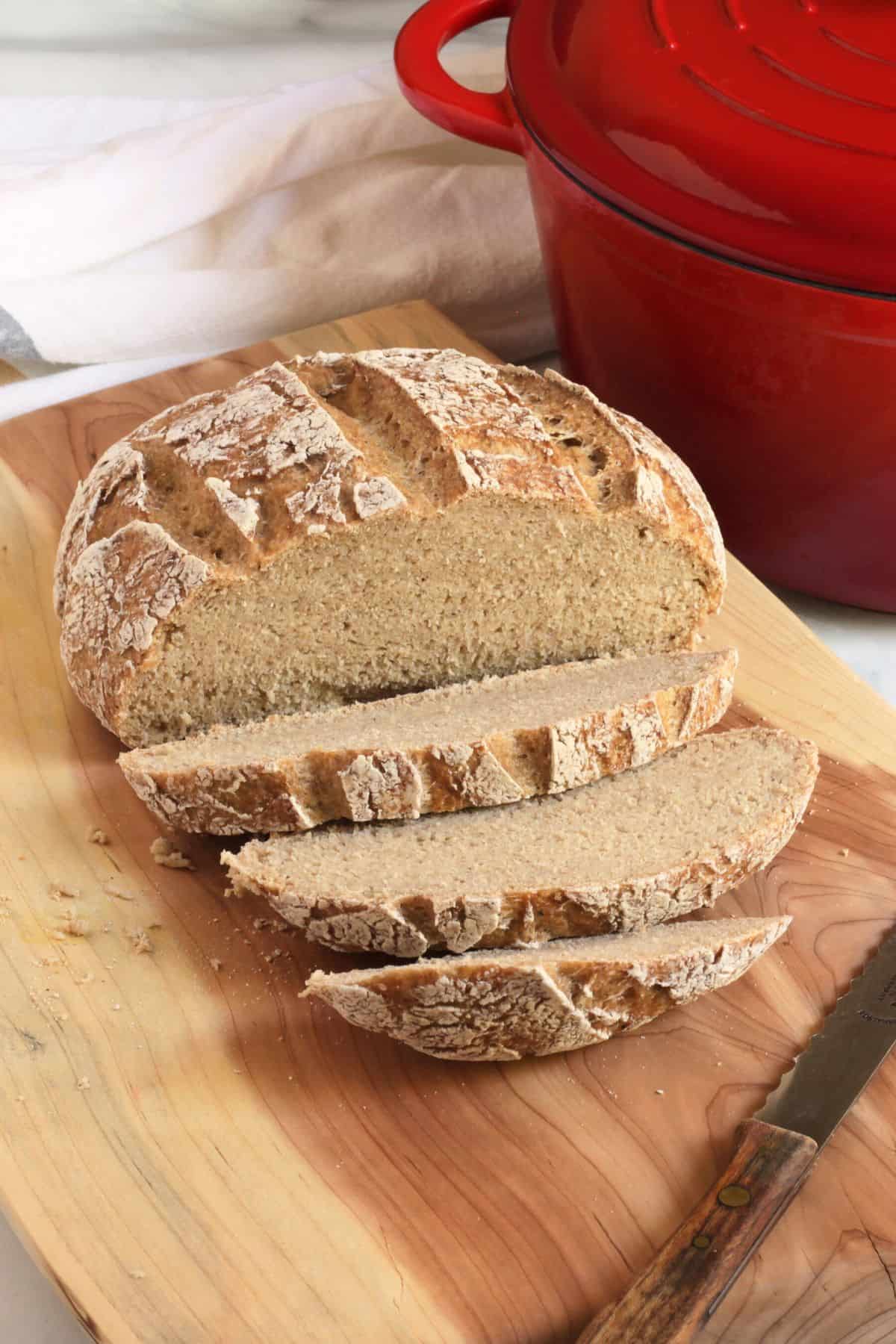 sliced, crusty round loaf of bread on wooden board.