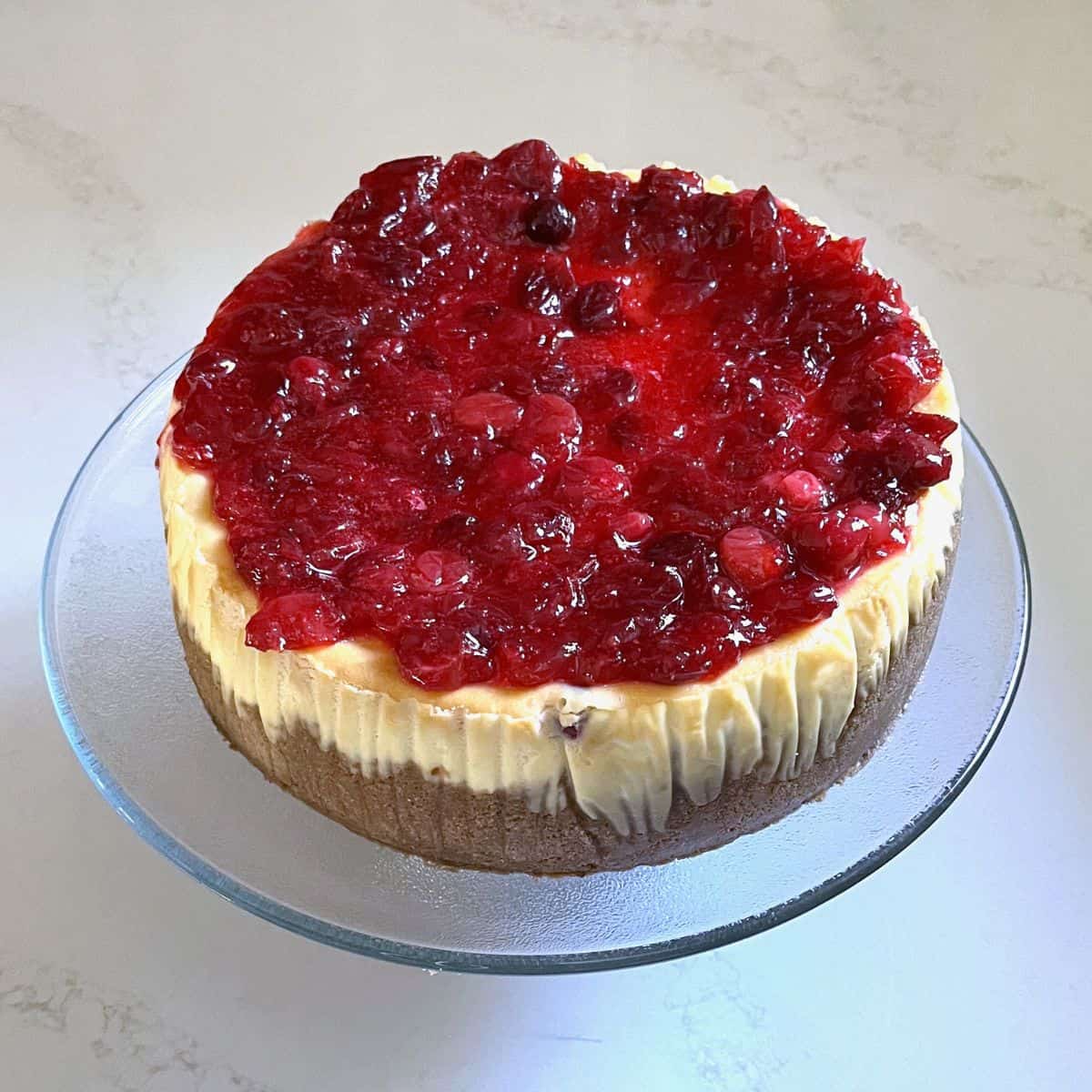 cheesecake removed from pan with cranberry sauce over the top.
