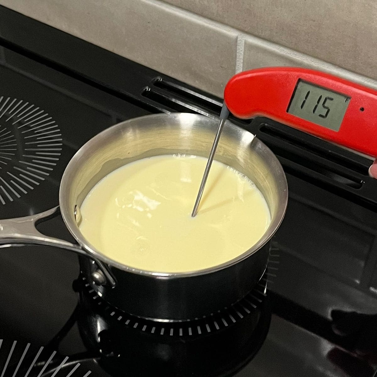 thermometer inserted into saucepan of milk reads 115 degrees.