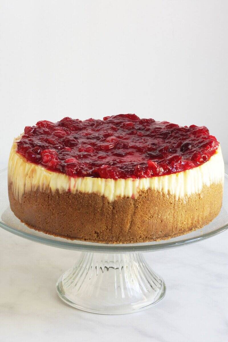 whole cranberry-topped cheesecake on glass pedestal stand.