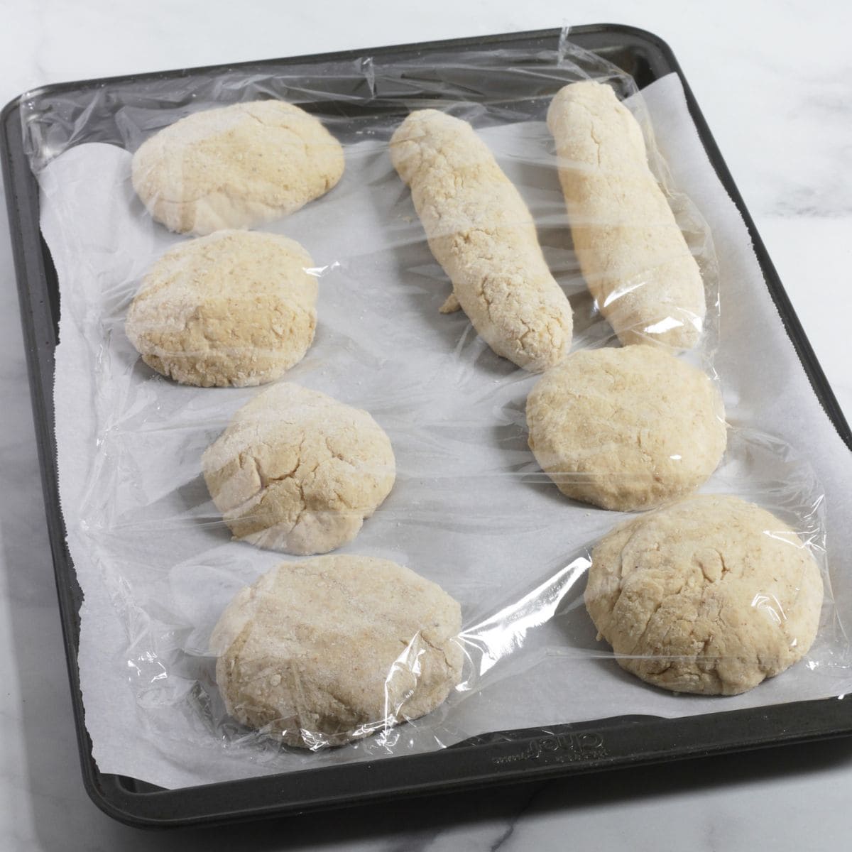unbaked buns on baking sheet covered in plastic.