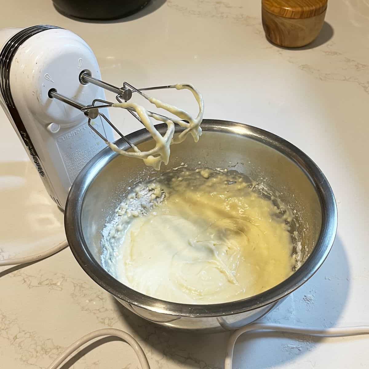 Batter, milk, and eggs being mixed with a hand mixer in a stainless steel bowl  at Cathy's Gluten Free.