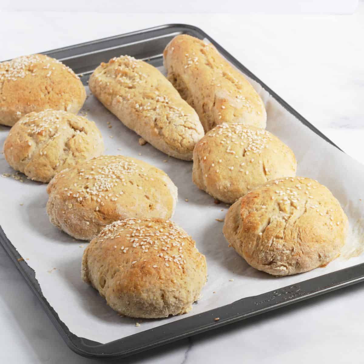 baked buns sprinkled with sesame seeds on a parchment lined tray.