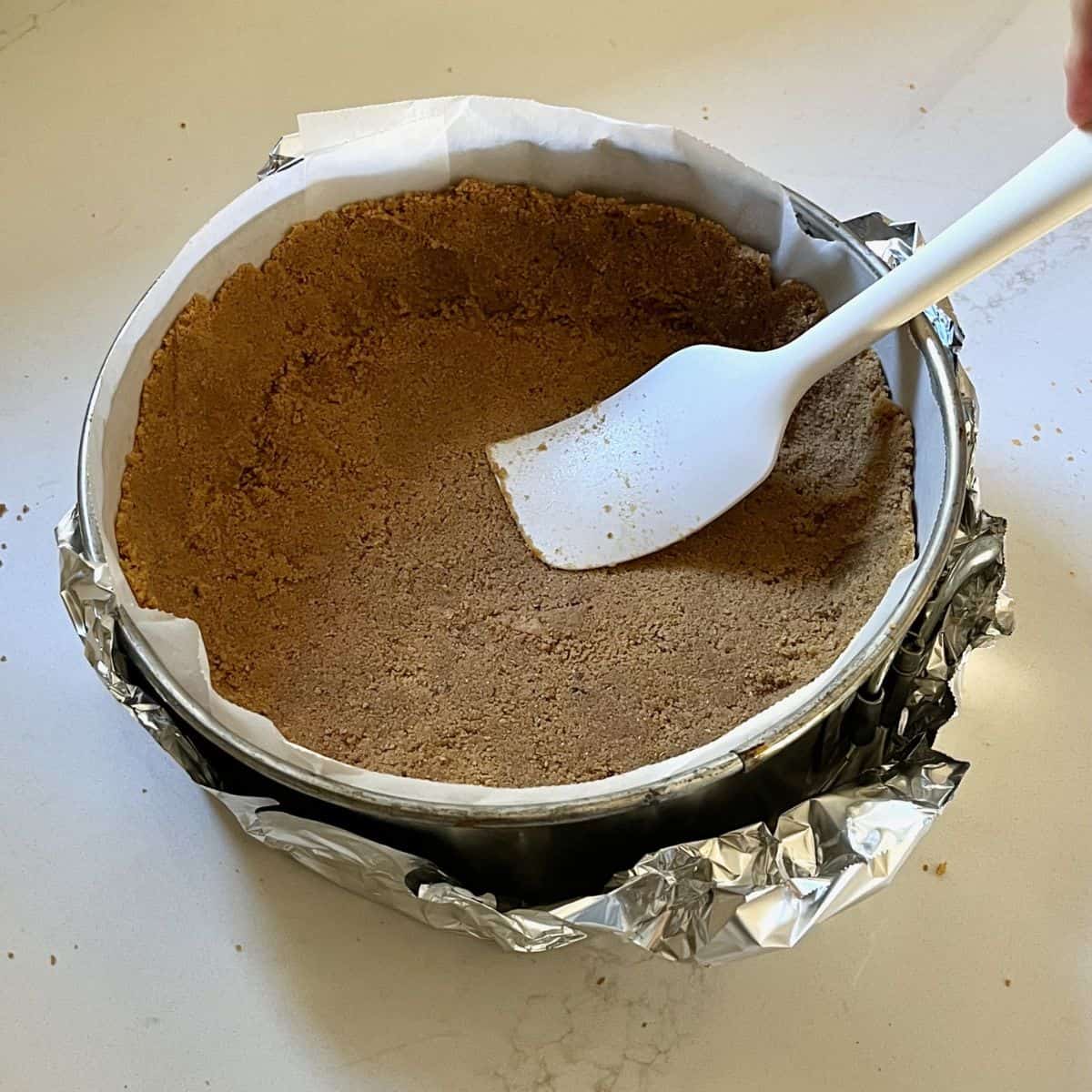 crumb mixture being pressed into a lined springform pan.