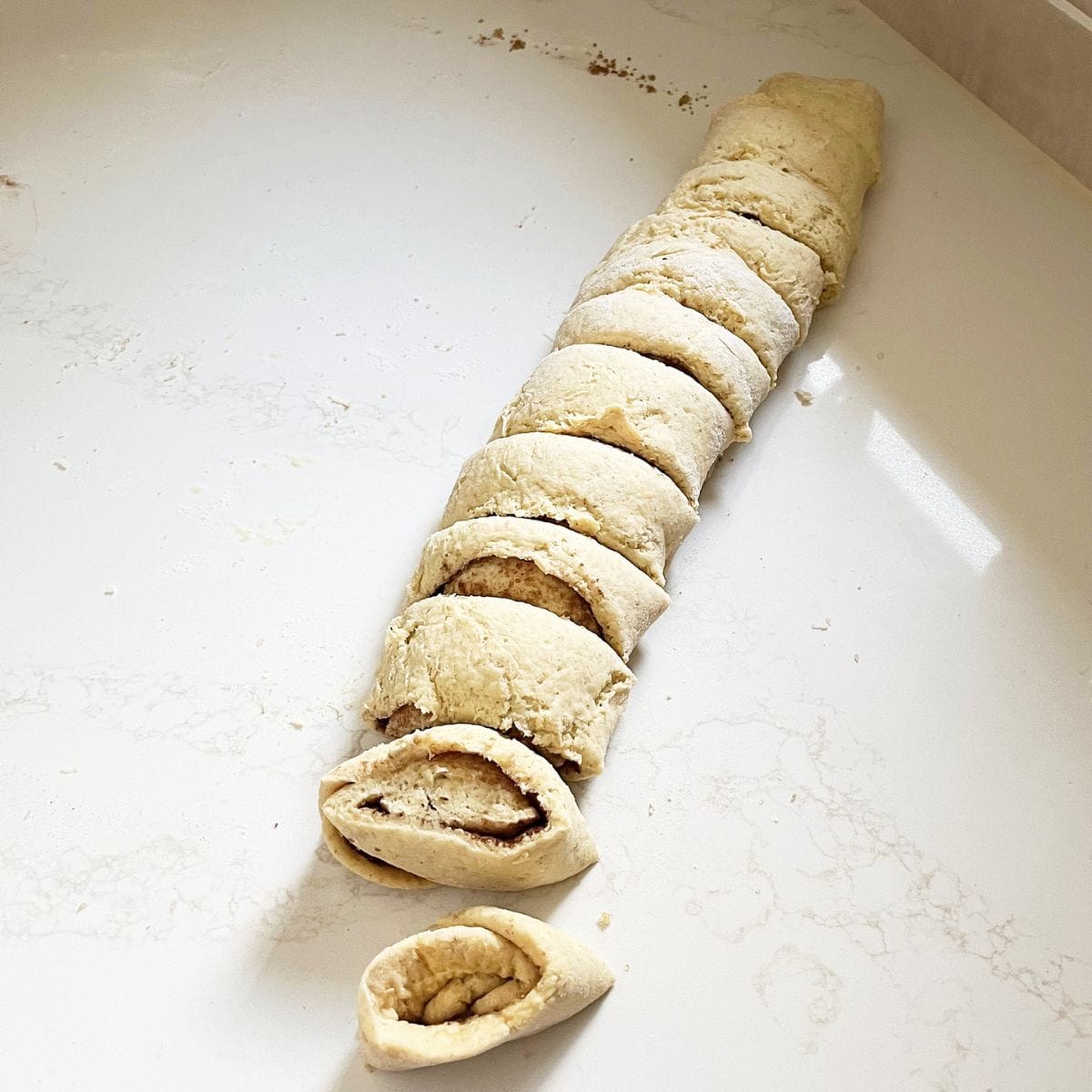 rolled dough is sliced, revealing sugar-cinnamon filling.