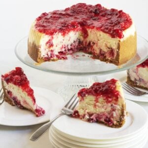 wedges of cheesecake with cranberry sauce dripping down over sides and remaining cake on glass stand in background.