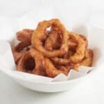 crispy, golden onion rings in white bowl.