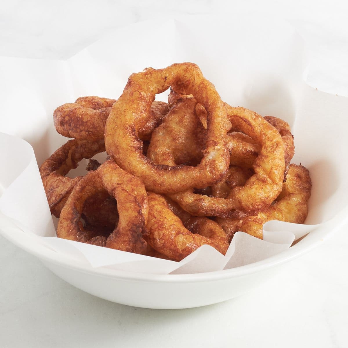 crispy, golden onion rings in white bowl.