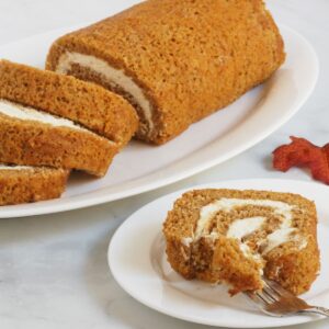 sliced pumpkin roll served on a white plate being eaten with a fork.