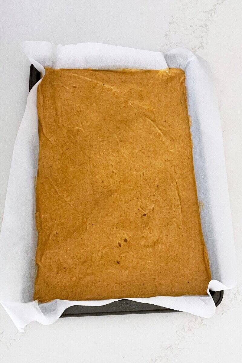 golden pumpkin batter spread into parchment-lined baking pan.