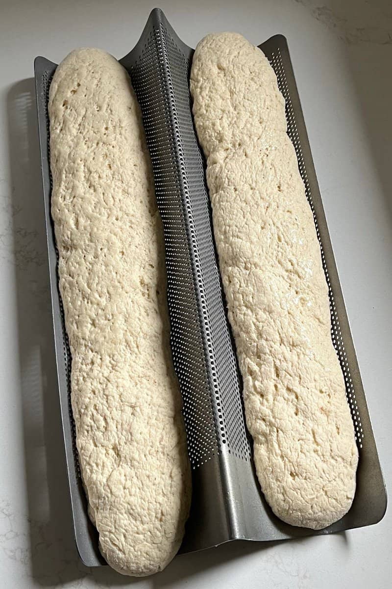 Fluffy gluten-free bread dough rising in a perforated baking pan, ready for baking.
