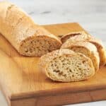 sliced crusty baguette on wooden cutting board.