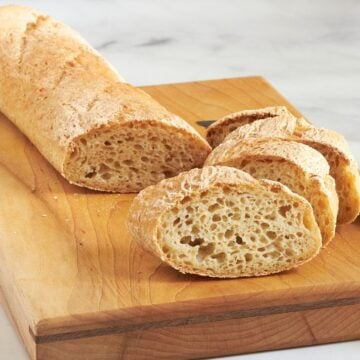 sliced crusty baguette on wooden cutting board.