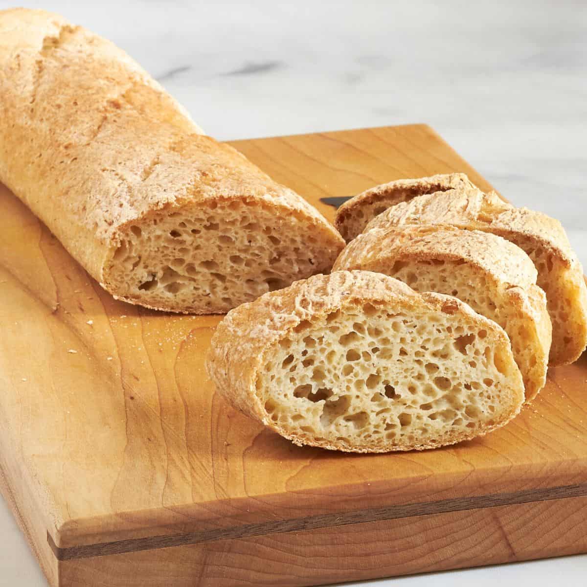 sliced crusty baguette on wooden cutting board.