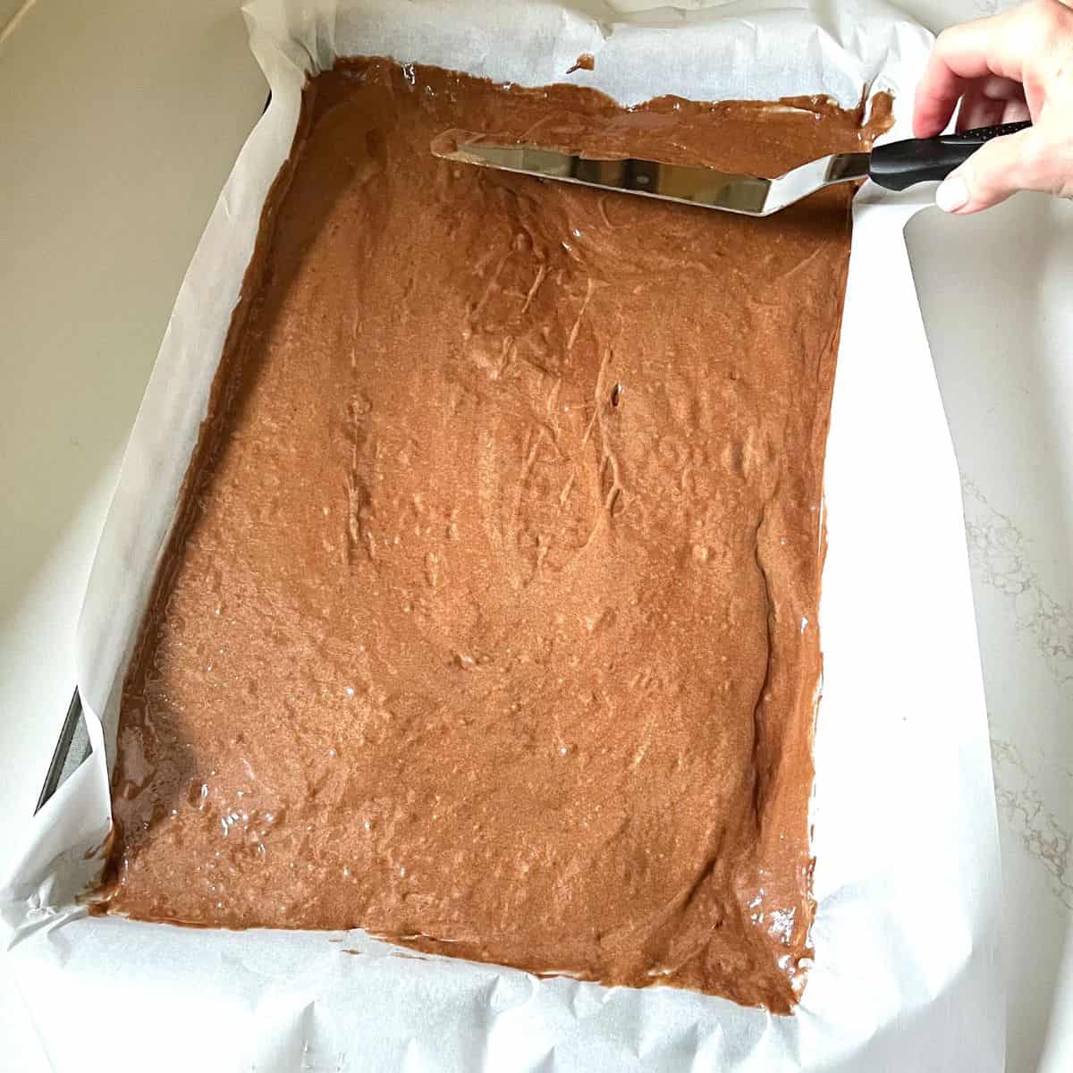 chocolate batter spread into parchment-lined baking pan with offset spatula.