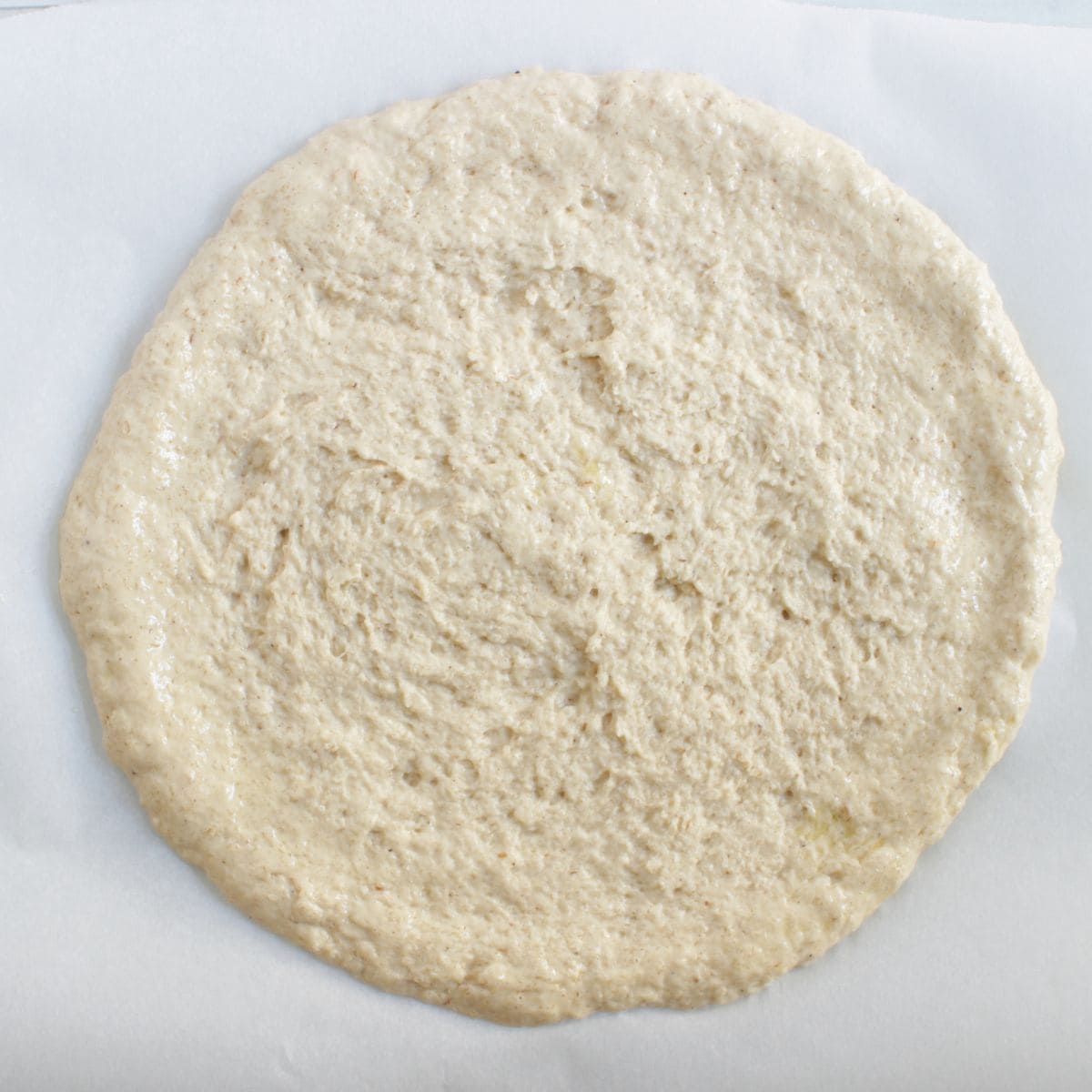 round, moist gluten-free pizza dough pressed into a circle on parchment paper.