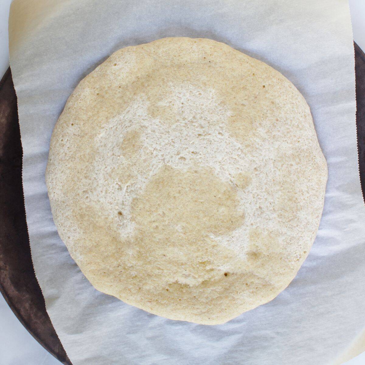 partially baked gluten-free pizza crust on parchment paper on pizza stone.