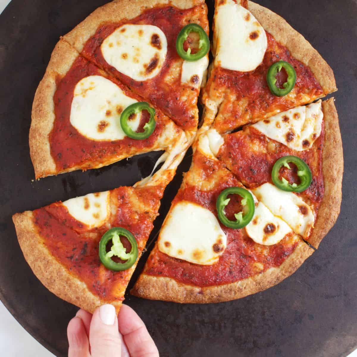 fingers lifting a wedge of browned gluten-free pizza from hot stone.